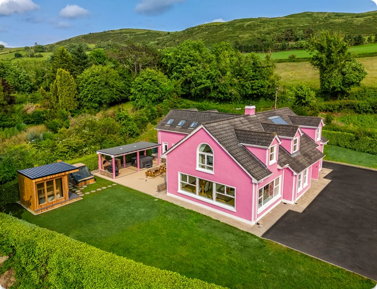 An image of Lily's Pink house taken from an aerial view showing the front and left side of the house with the sauna, plunge pool, driveway, and outdoor relaxation area in one photo.
