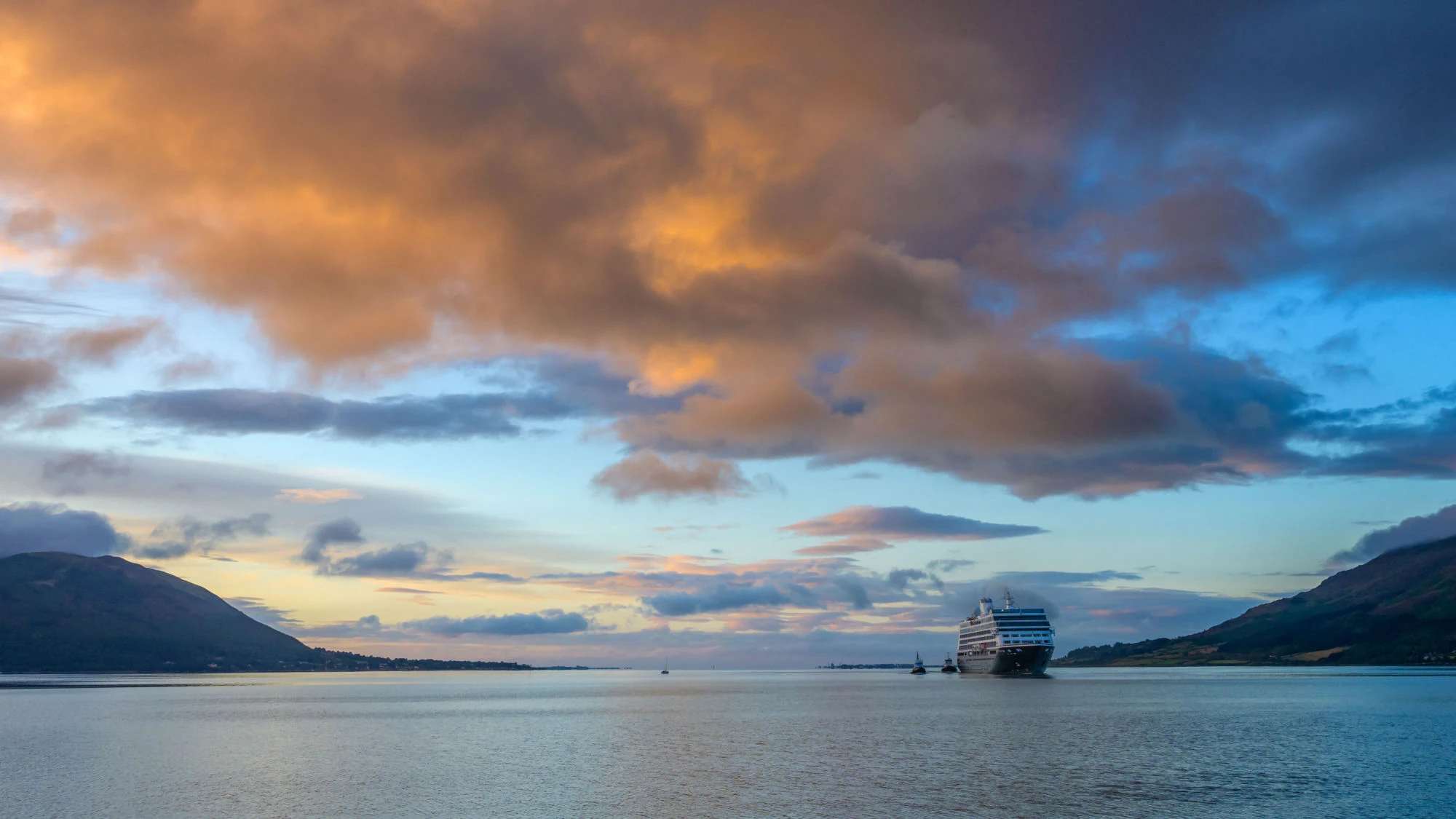 An image of a cruise liner approaching Warrenpoint around sunset time with calm water and the mourne mountains flanking each side