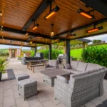 An image of Rosie's cottage outdoor relaxation area with a grill, couches, table, hot tub, and bench.