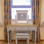 Vanity in a bedroom at Lily's Pink house with a mirror, drawers, and stool