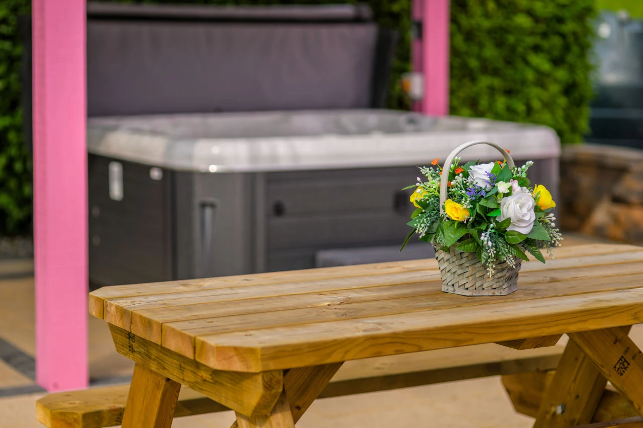 An image of some flowers on the wooden bench at Lily's Pink House with a hot tub in the background.