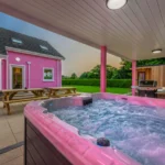 An image of the view from next to the hot tub at Lily's Pink House showcasing the sunset, back entrance into the house, grill, plunge pool, and sauna.