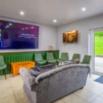 An image showcasing one of the relaxation areas in the house with a dart board, a large TV, a couch, and many different chairs around the room.
