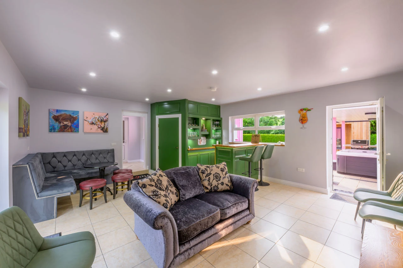 Another image of Lily's Pink house bar area with the various seating options and an open door leading to the outdoor hot tub and outdoors relaxation area.