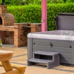 An image of Lily's Pink House hot tub with one of the benches in the foreground and the brick pizza oven in the background on the left