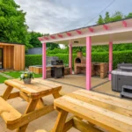 An image outside of Lily's Pink House showing the entire relaxation area with two benches in the foreground, the covered hot tub, grill, and pizza oven on the right hand side of the background